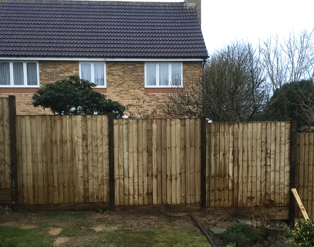 Wooden fence in front of a brick house with trees behind it