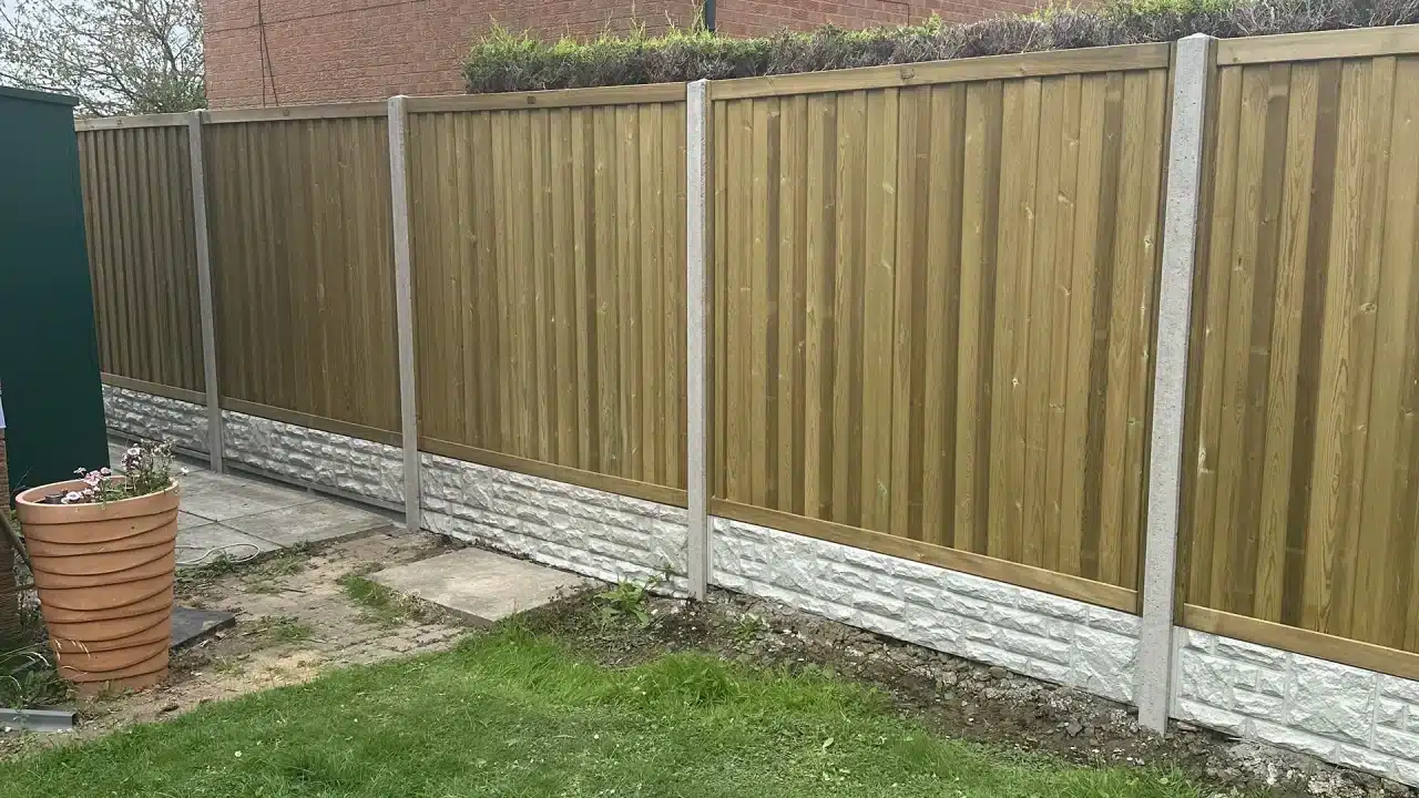 New wooden garden fence with concrete posts and a stone base, beside a patio and flower pot