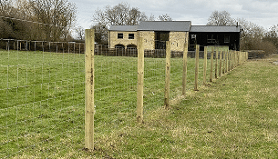 Fence posts and wire mesh enclosing a grassy field beside a small building