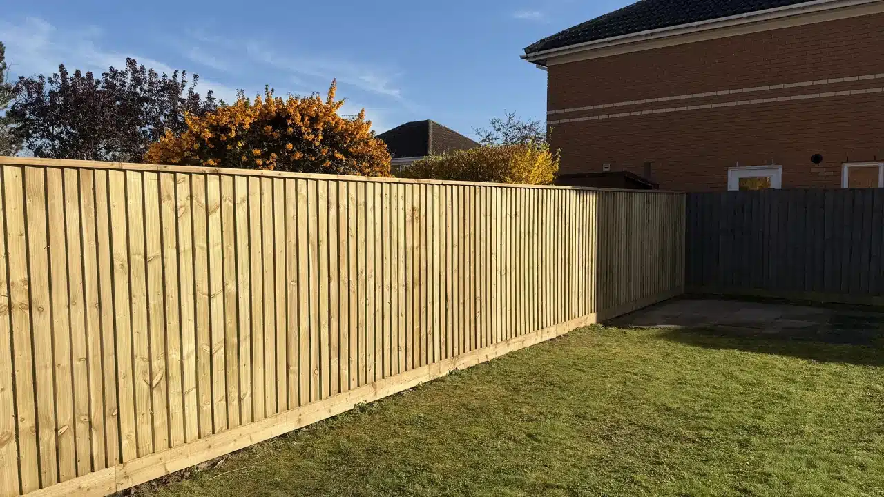 New wooden garden fence beside a lawn and patio, with houses and trees behind