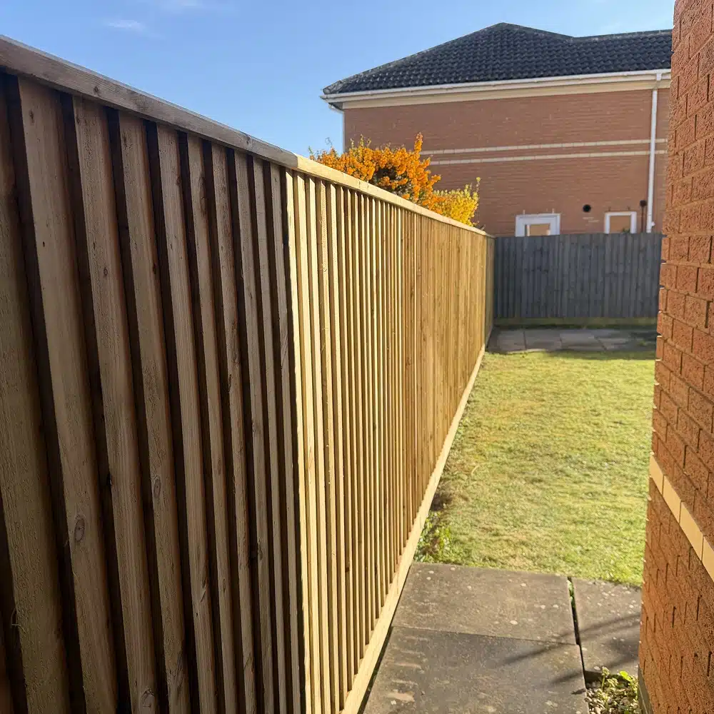 Wooden garden fence beside a paved path and lawn, with houses in the background
