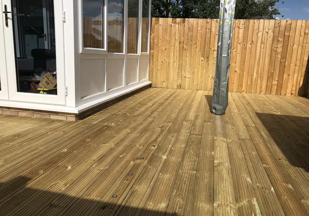 Wooden patio decking beside a conservatory, with a fenced garden and covered post