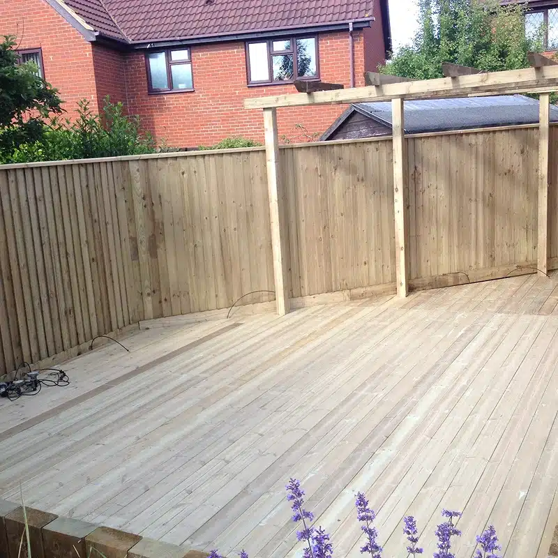 Wooden deck under construction in a back garden, with fencing and a pergola frame