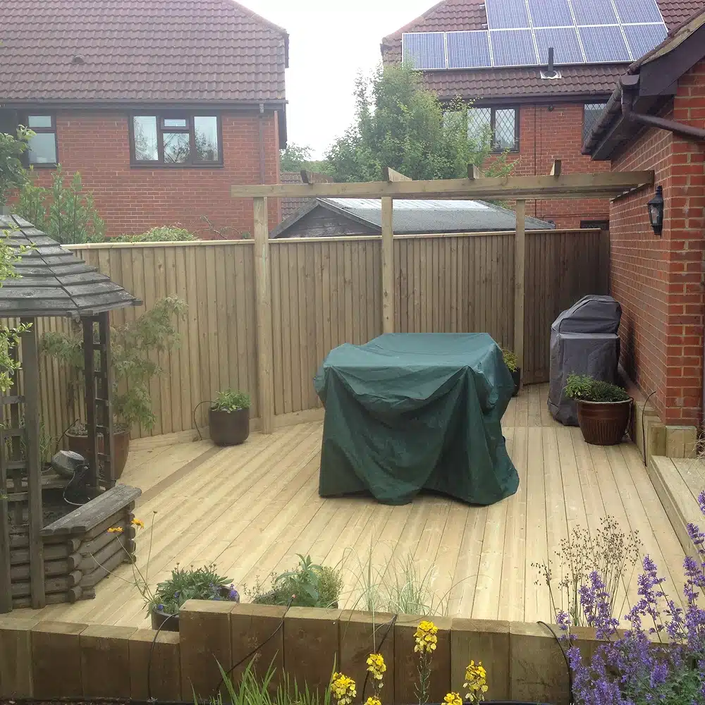 Back garden with a wooden deck, covered table, potted plants and solar panels on the roof