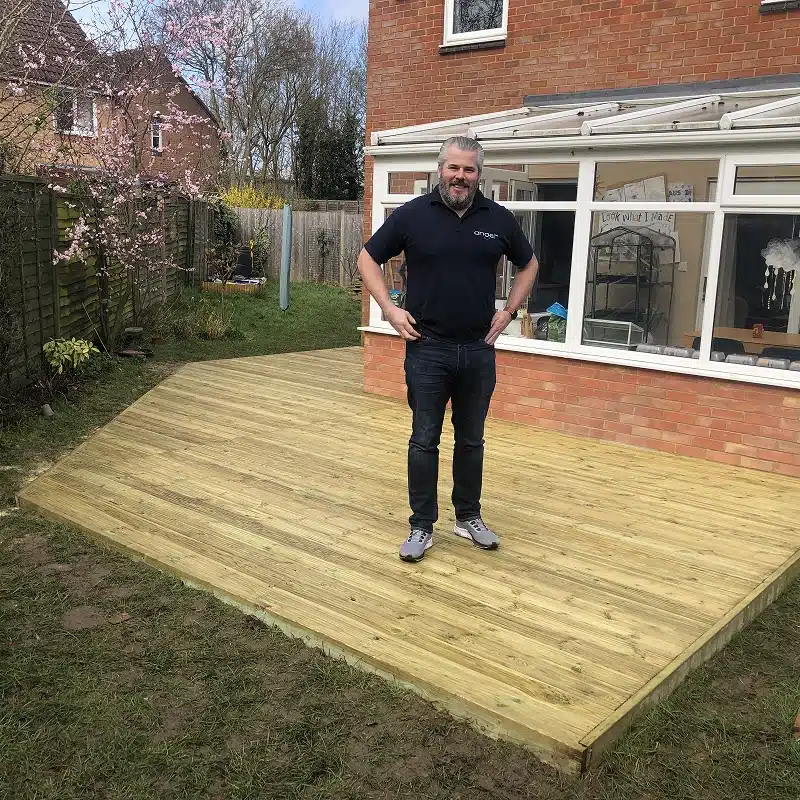 Man standing on a newly built wooden garden deck beside a house