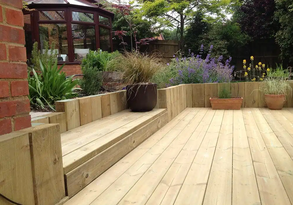 Wooden garden decking with raised planters and potted plants beside a conservatory