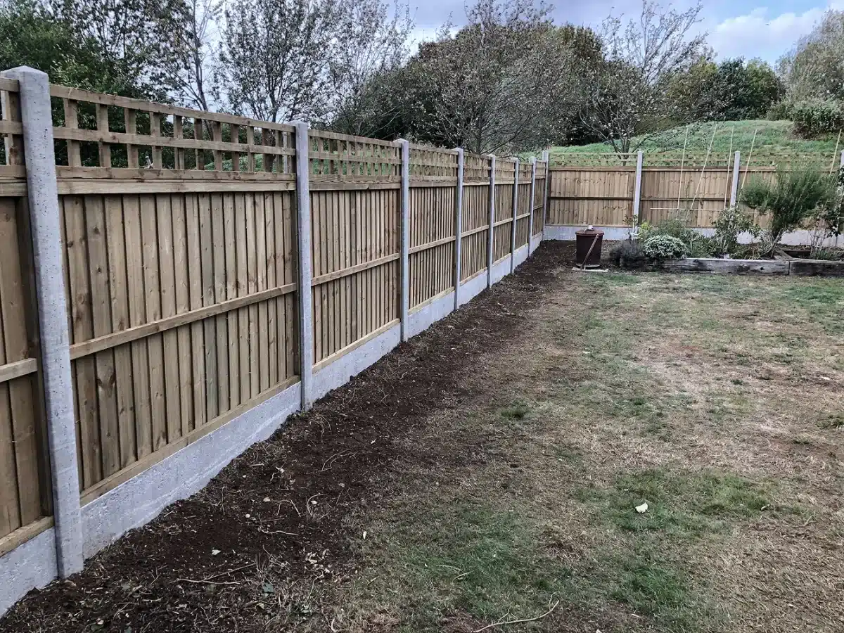 New wooden fence along the garden boundary with a strip of bare soil beside the lawn