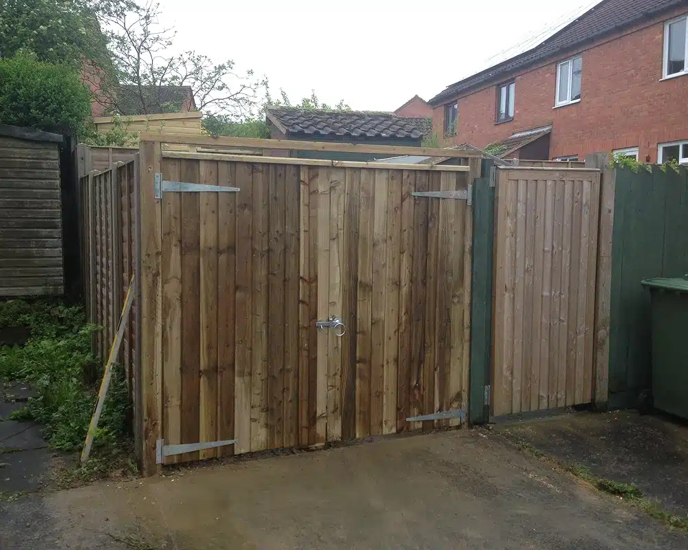 Wooden double gates with a side gate in a driveway, with houses behind
