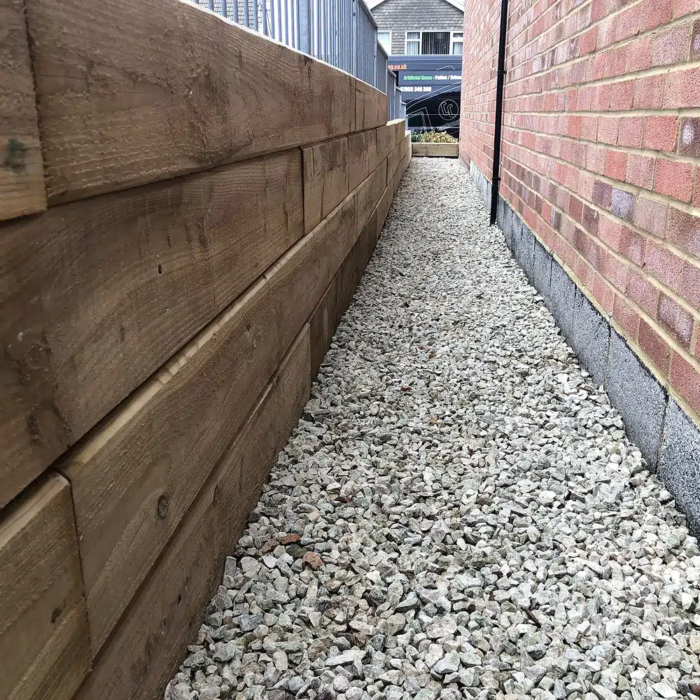 Narrow gravel path between a timber retaining wall and a brick house wall