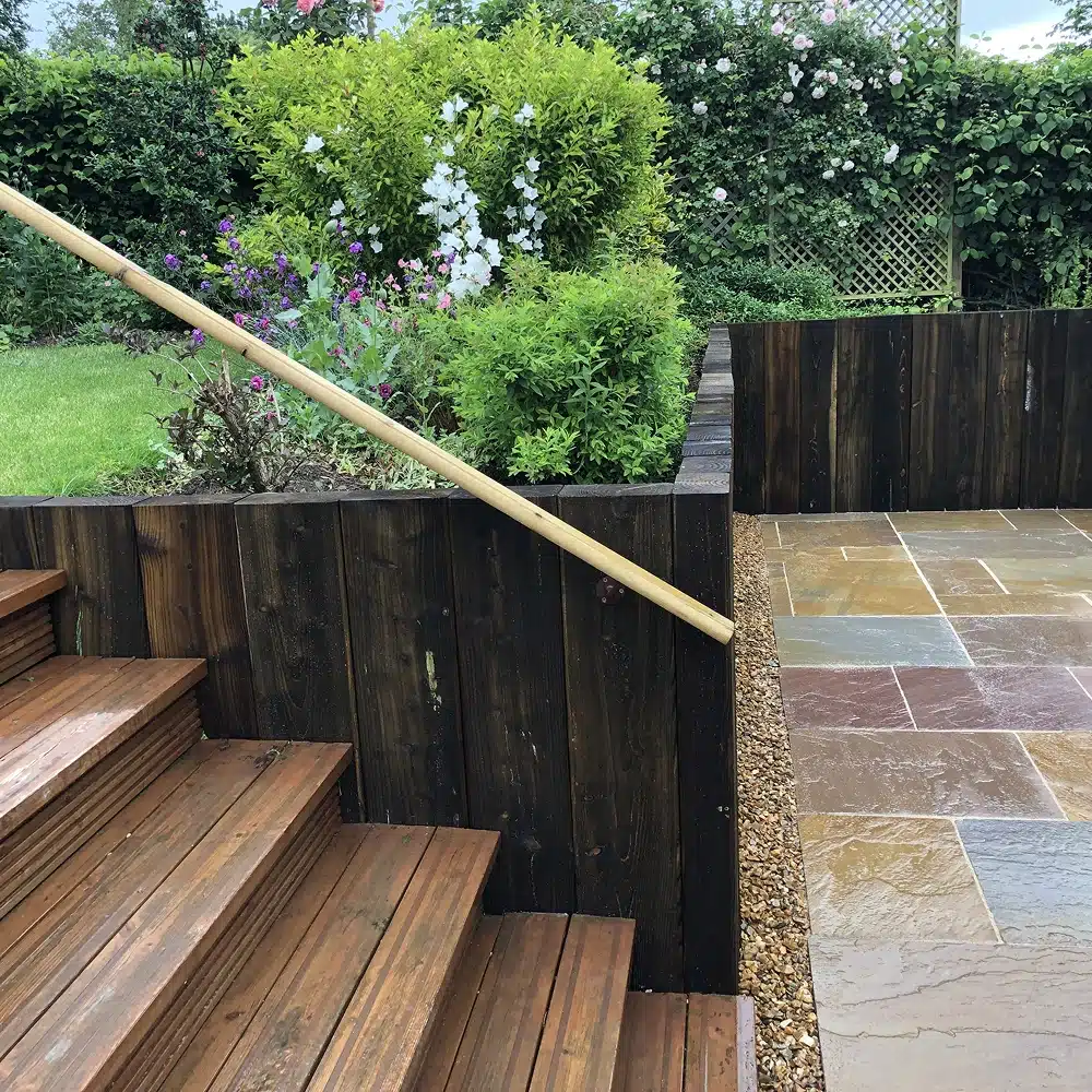 Wooden garden steps beside a paved patio and planted border with shrubs and flowers