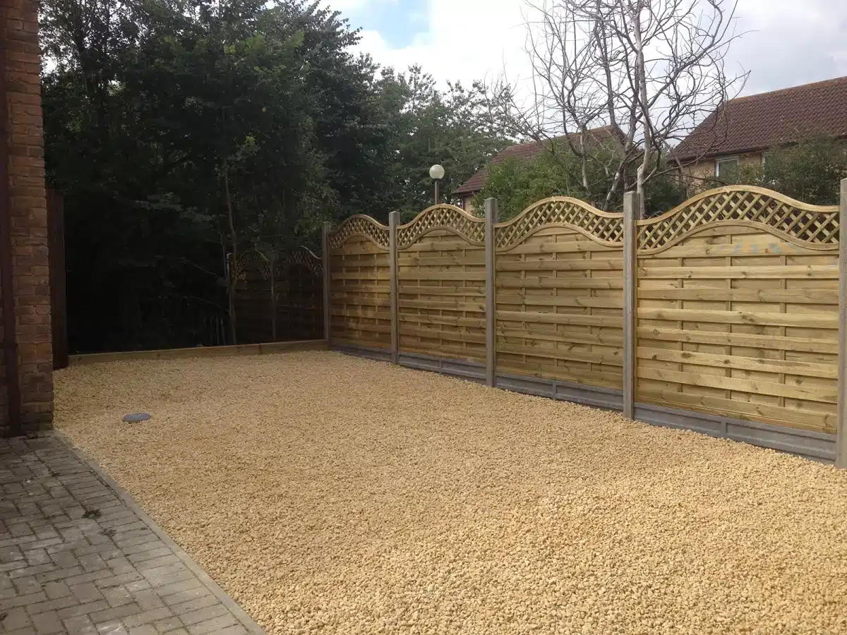 Gravel-covered garden area with a wooden fence and paved path beside a brick building
