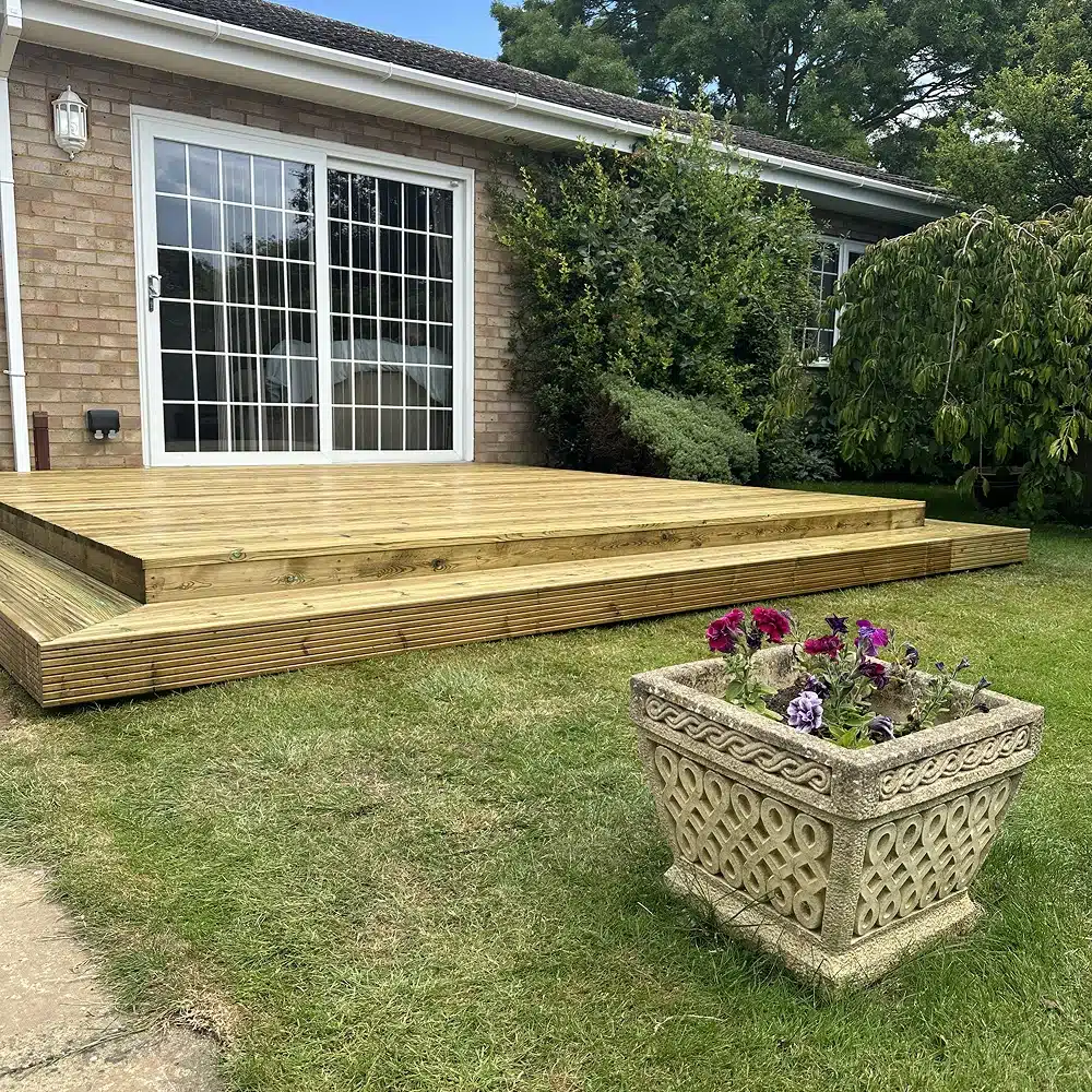 Wooden deck outside a house, with a flower planter on the lawn