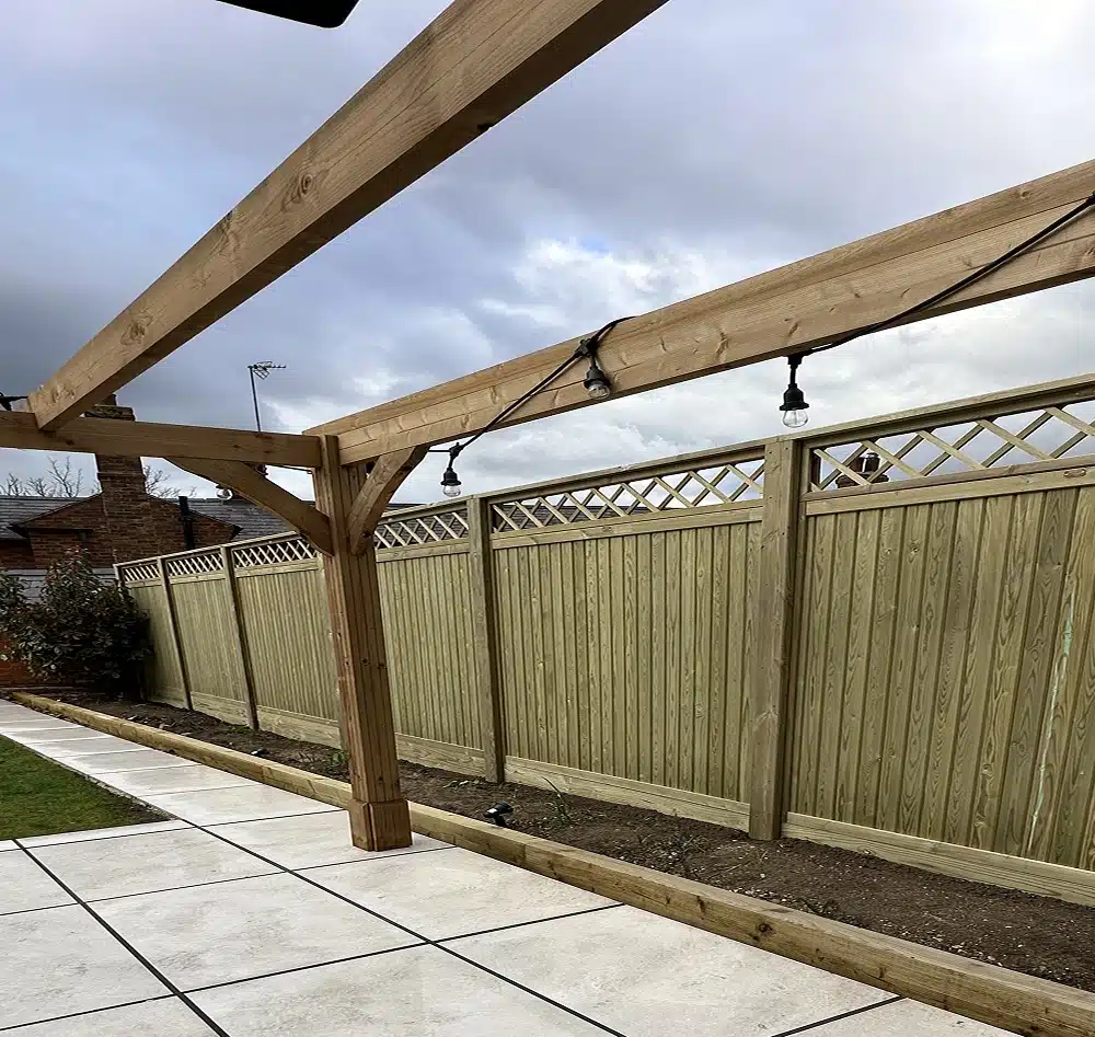 Wooden pergola over a paved patio beside a fenced garden