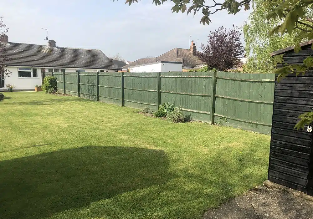 Back garden with a lawn, green fence and neighbouring houses beyond
