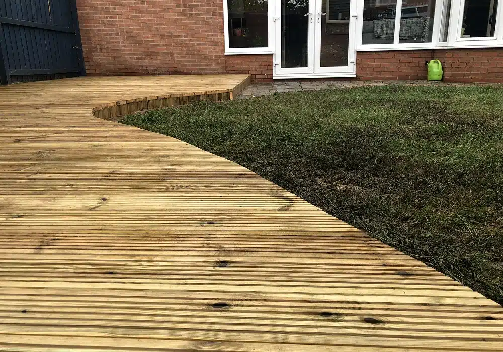 Curved wooden deck beside a lawn outside a brick house