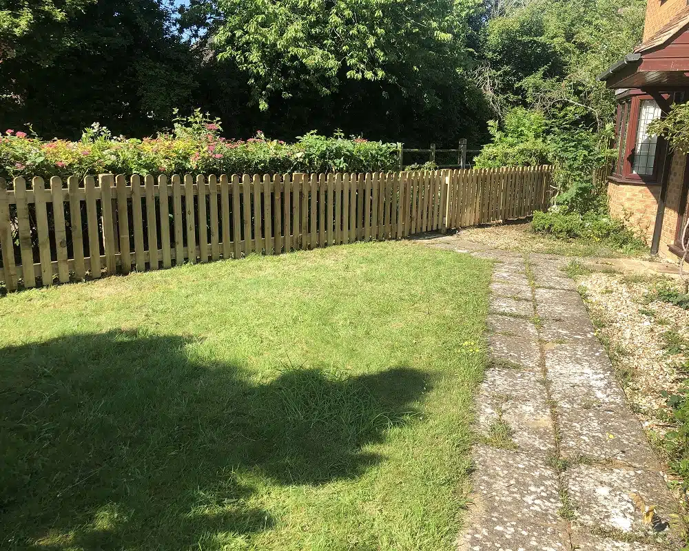 Sunny garden with lawn, picket fence and a stone path beside a house