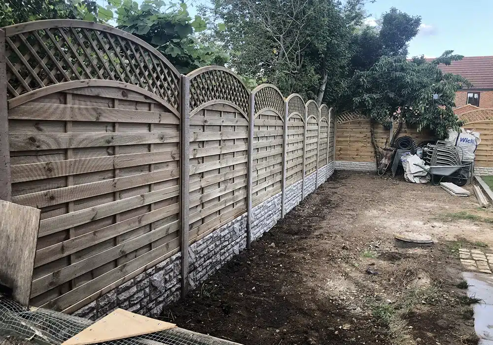 New wooden garden fence with arched trellis panels along the boundary of a bare back garden