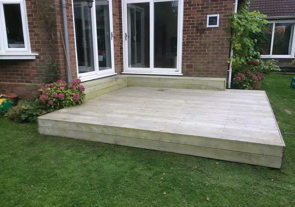 Raised wooden patio deck in a garden beside a brick house