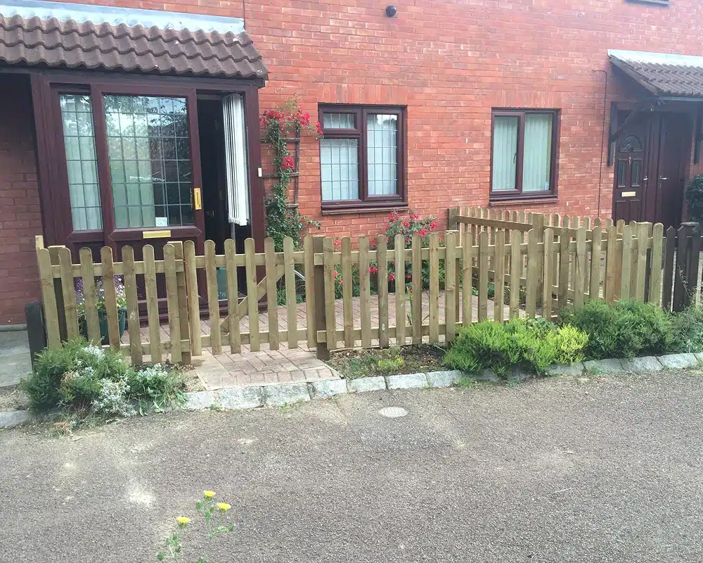 Front garden with a wooden picket fence in front of a brick house