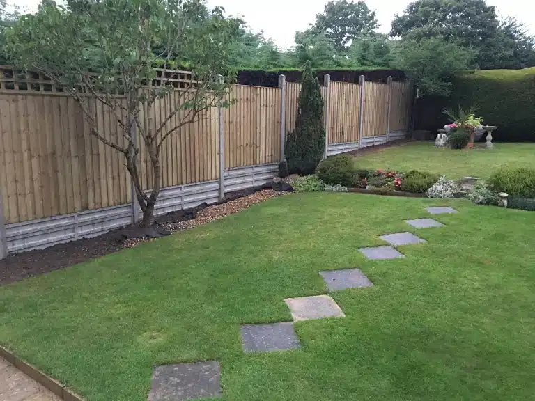 Back garden with lawn, stepping stones, wooden fence and planted borders