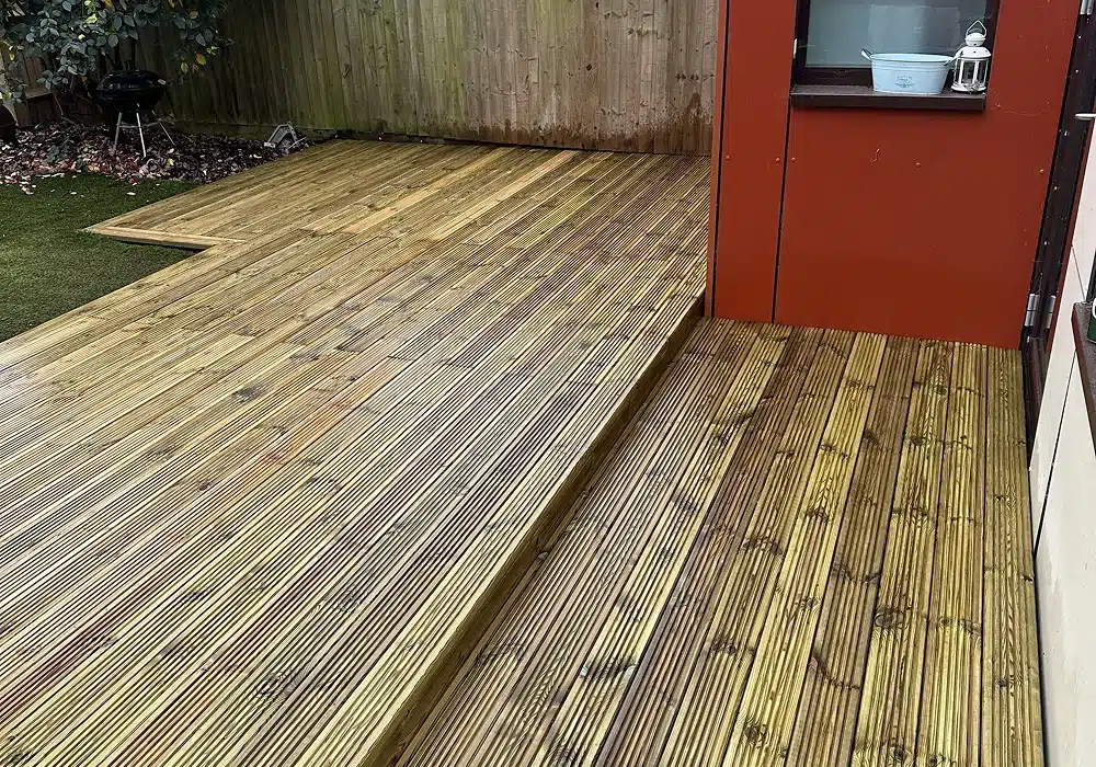 Timber garden decking with a raised platform beside a red shed and fence