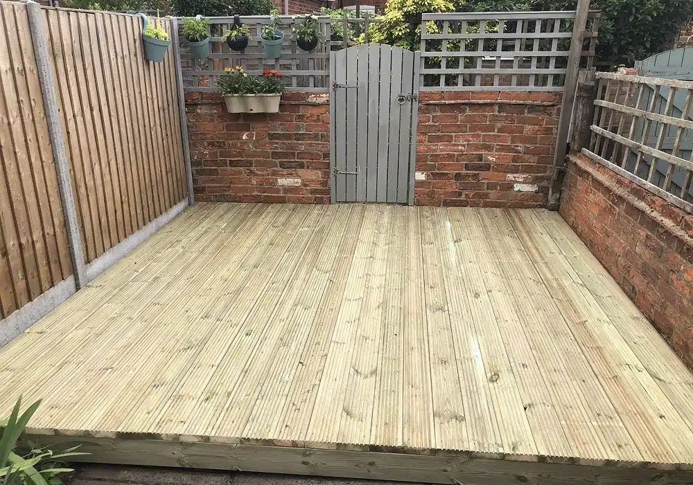 Empty wooden garden deck with a grey gate and brick wall planters at the back