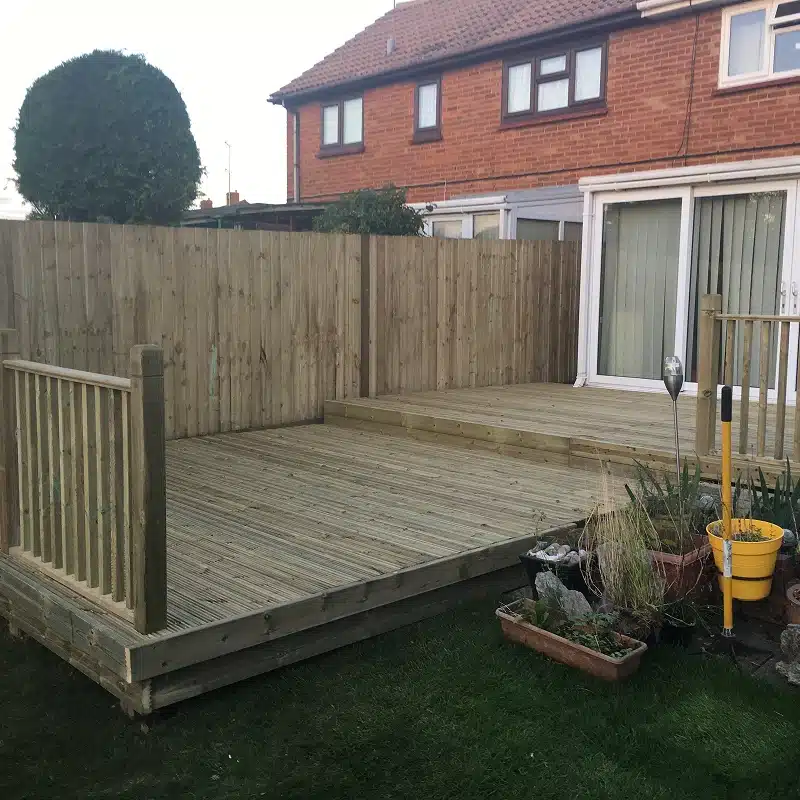 Wooden garden decking with a raised platform and fenced boundary beside a house