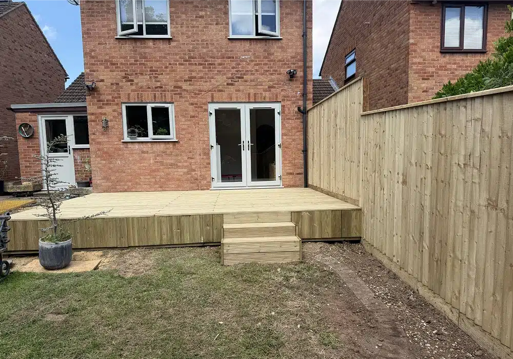 Rear garden with a raised timber deck, steps and new wooden fencing behind a brick house