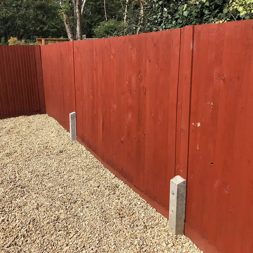 Red wooden fence beside a gravel path, with concrete fence posts