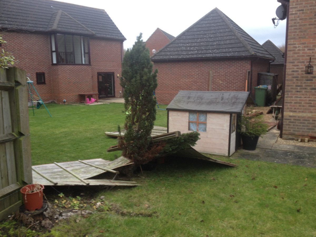 Back garden with a collapsed wooden fence panel and a small playhouse beside a lawn